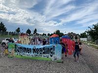Children marching in a parade holding a Summer Reading sign