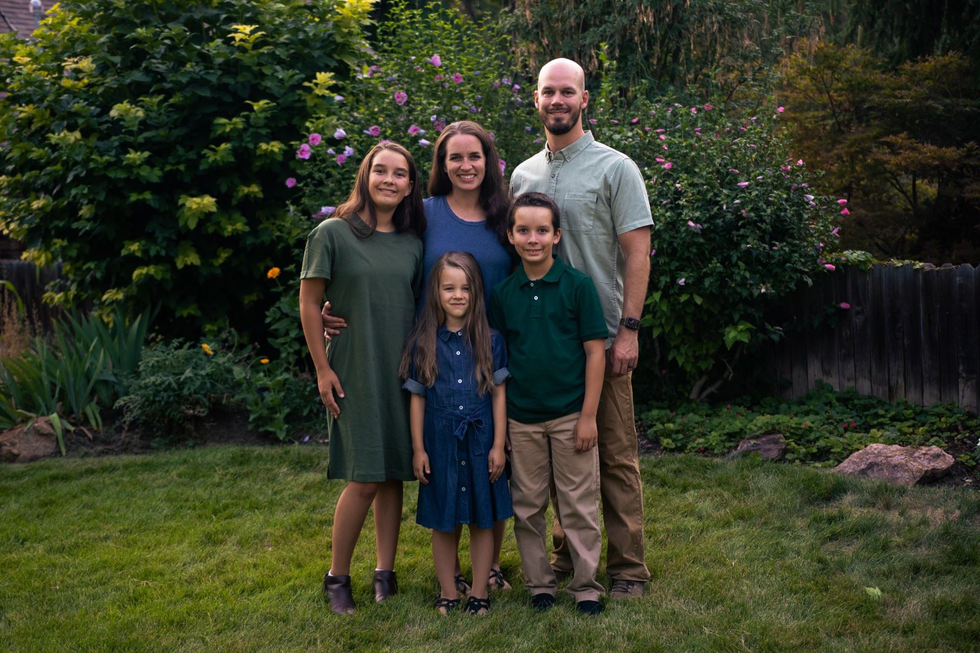 The Hunt family smiling in front of a landscaped area with flowers Opens in new window